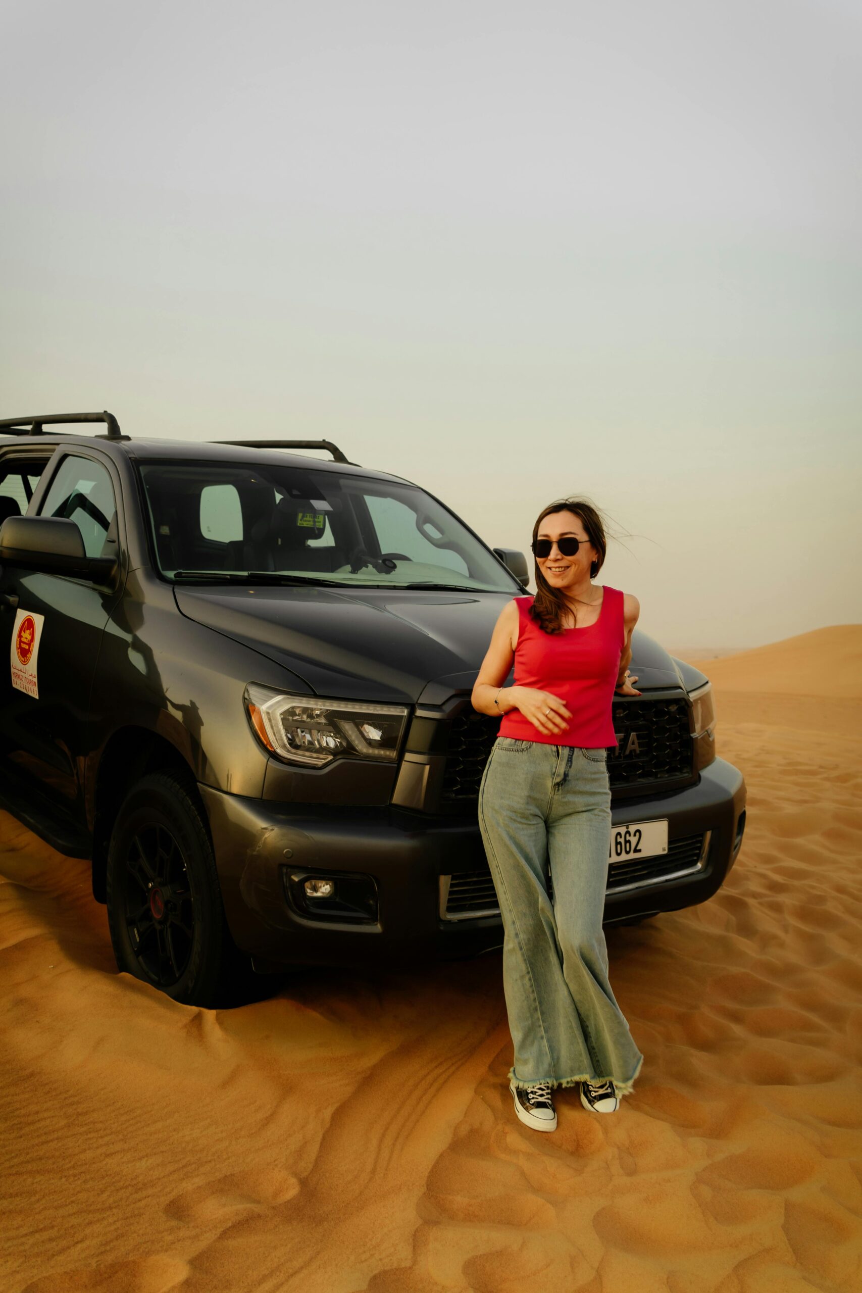 Woman leaning on SUV in sunny desert scene, showcasing adventure and travel vibes.